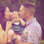 Happy family moment: mother and father lovingly kiss their smiling baby girl on the cheeks. A warm, intimate family portrait.