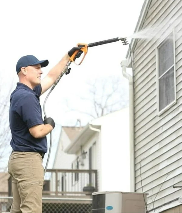 A man points a pressure washing wand at house siding.