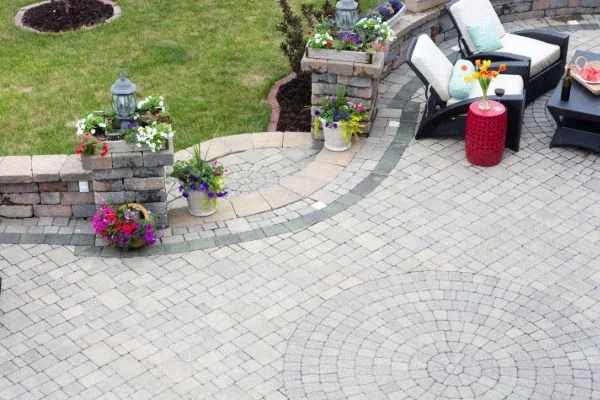 A curved stone patio surrounds garden planters and outdoor furniture.