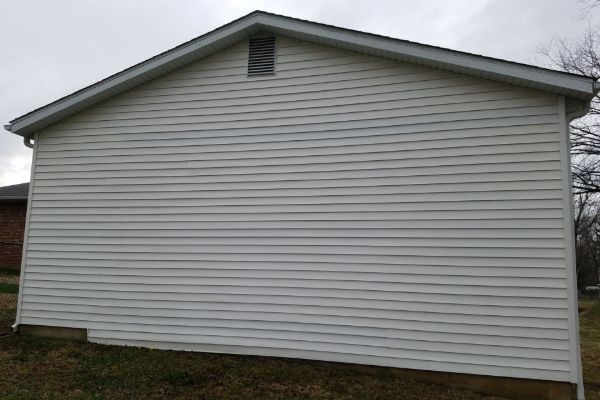 Side view of a white vinyl-sided house under a cloudy sky, showcasing the need for house washing to remove grime and stains.