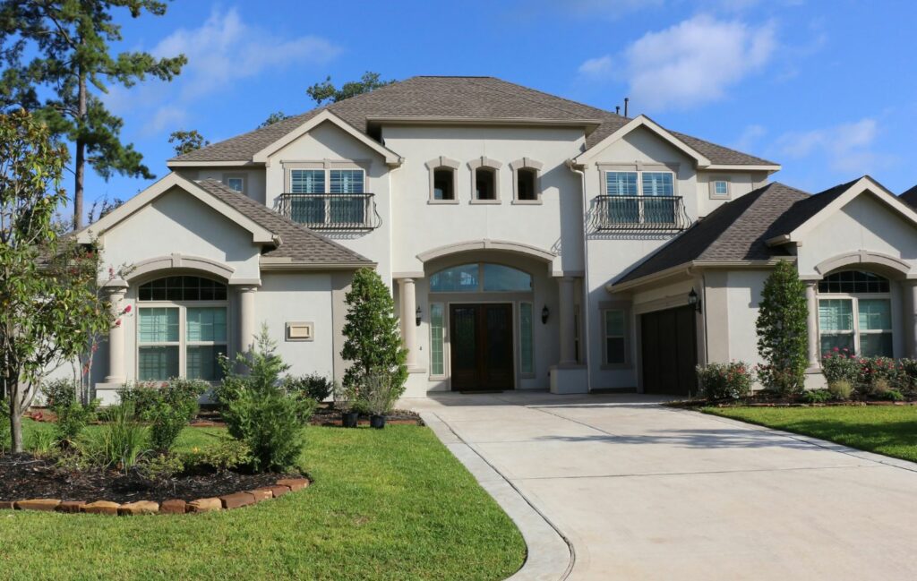 Elegant two-story stucco home with a well-manicured lawn and driveway. The house features a symmetrical design, arched windows, and small balconies, showcasing a beautiful residential property.