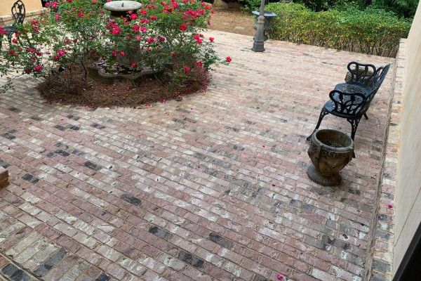 Brick patio with a central fountain surrounded by red roses. A dark metal bench sits to the side, offering a place to relax in this tranquil garden gallery setting.