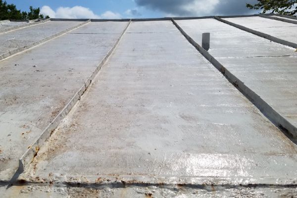 Close-up of a low-slope metal roof after roof cleaning. The surface is light gray with vertical seams. Some rust and debris are visible at the edges.