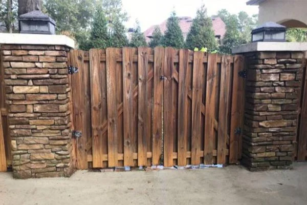 A brown wooden gate stands between two stone clad pillars.