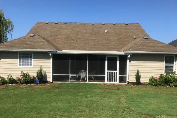 A brown house roof overlooks a screened porch and lawn.
