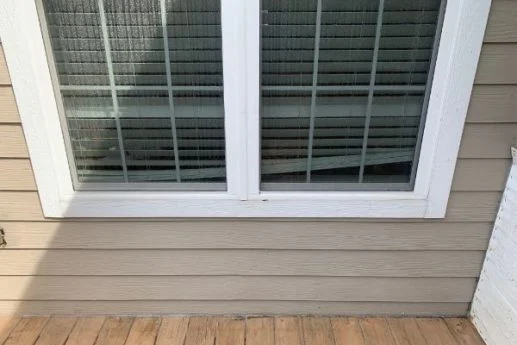 Clean beige siding runs beneath a white framed double window.