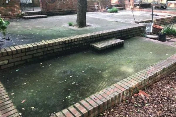 Green stains cover a sunken patio enclosed by brick walls.