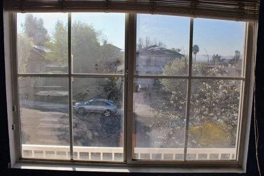 A hazy window partially obscures houses and a parked vehicle.