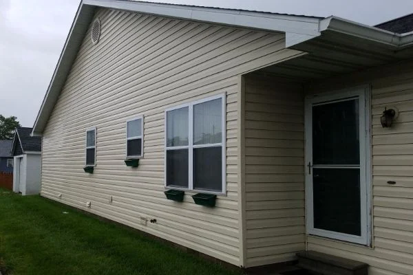 Light siding surrounds windows and a doorway beside green grass.