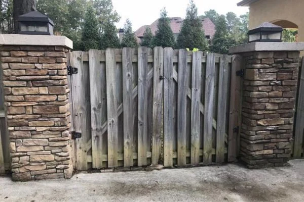 A gray wooden gate stands between two stone clad pillars.