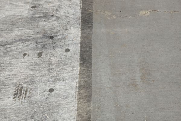 Contrasting textures on a concrete surface, one side weathered with dark stains and tire marks, the other a smooth, clean gray with a subtle crack.