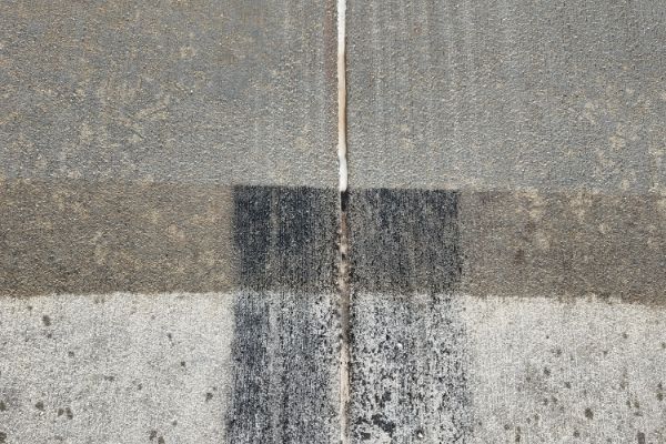 Overhead view of gray concrete slabs divided by a narrow white line. Weathered textures and dark tire tracks add visual interest.