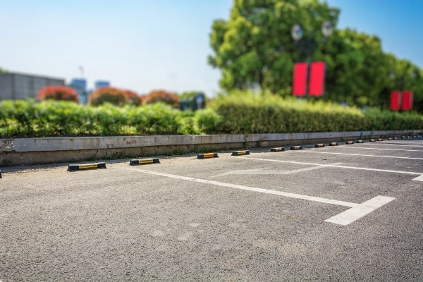 Empty parking lot with white lines, wheel stops, and green landscaping in the background. Shows the clean surface after parking lot power sweeping.