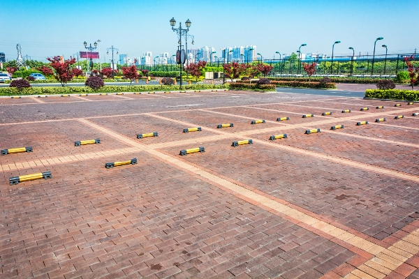 Expansive brick parking lot with rows of parking bumpers under a clear blue sky, ideal for parking lot power sweeping. City buildings visible in the background.