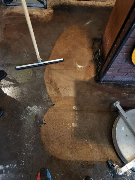 A long handled squeegee rests on a wet entryway floor.