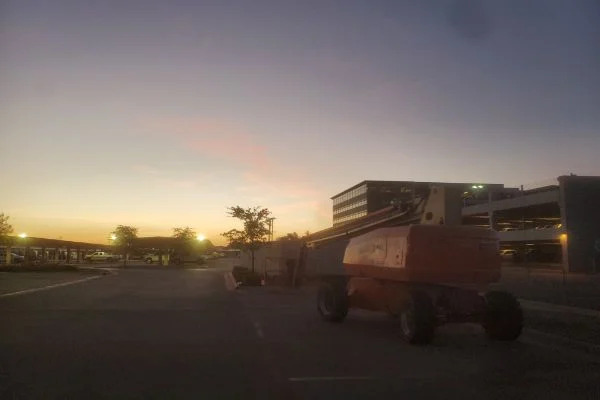 A wheeled lift stands beside a building at dusk.