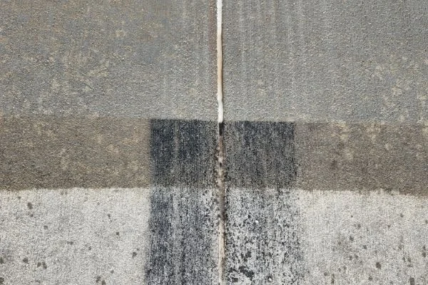 A narrow spray line crosses contrasting patches of concrete pavement.