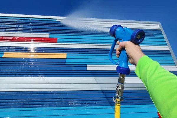 A blue spray nozzle directs water across a striped metal wall.