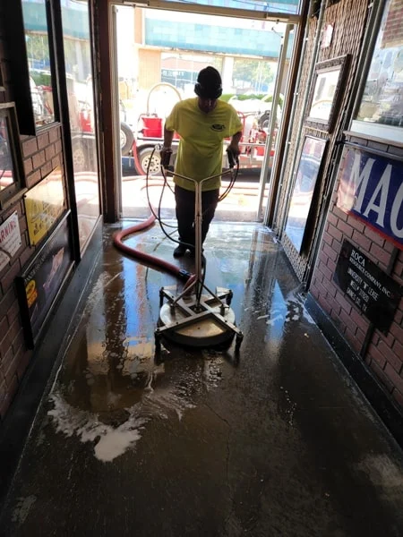 A worker uses a surface cleaner inside a wet storefront entrance.