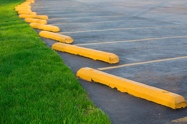 Parking lot with bright yellow parking bumpers lining the asphalt, next to a strip of green grass. The scene evokes a clean and organized space, ready for parking lot power sweeping.