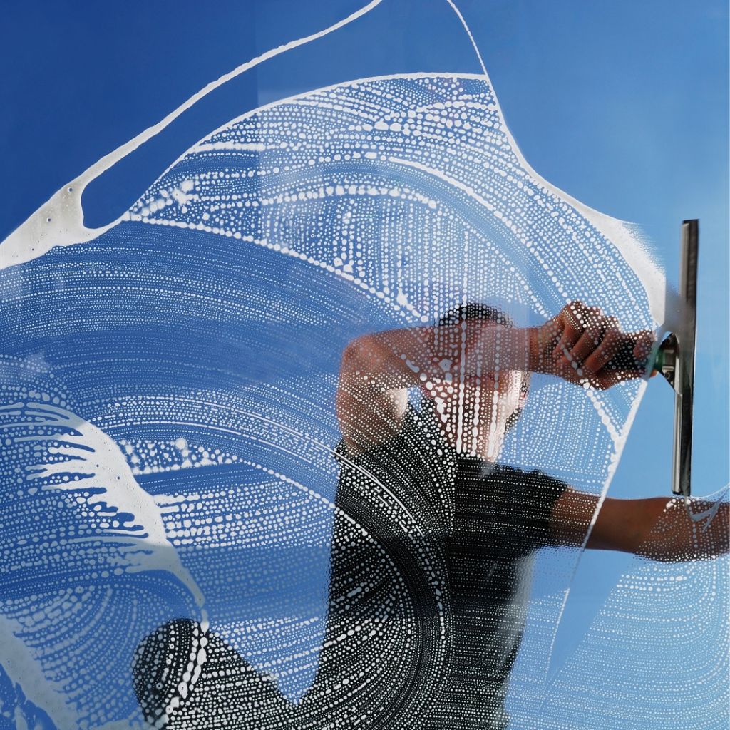 A window cleaner uses a squeegee on a soapy window, revealing a clear blue sky in Odessa, Texas. Professional window cleaning by Atlas Scrubbed.