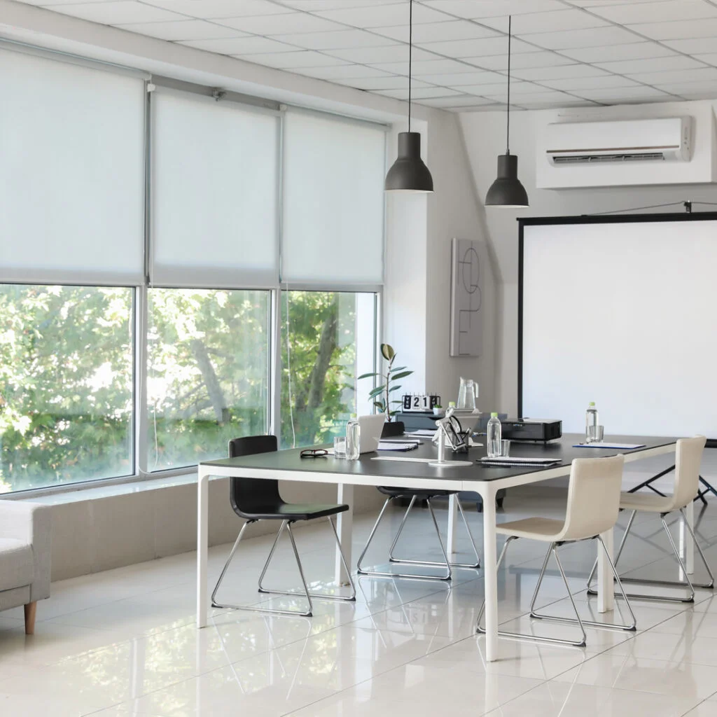A bright office meeting area contains a table and white chairs.