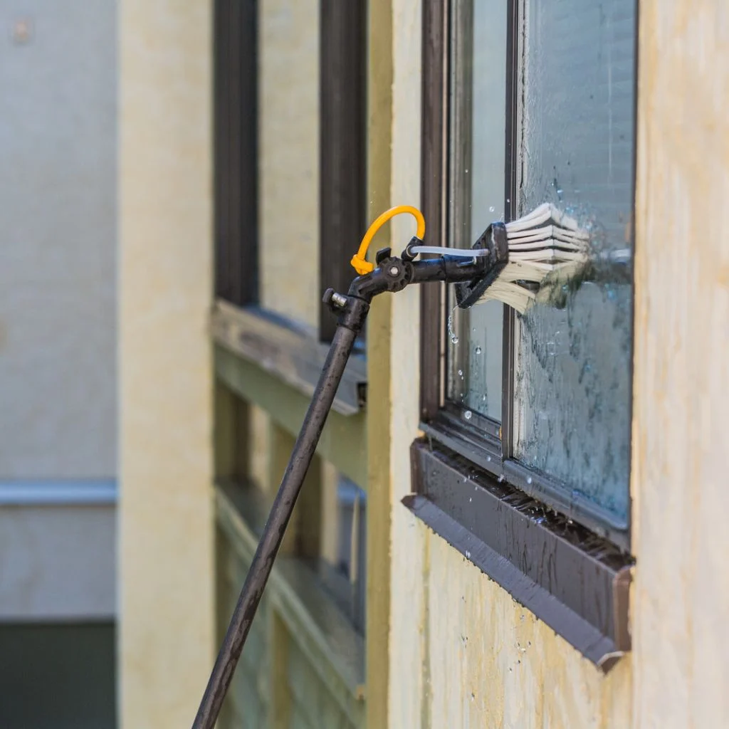 A brush on a long pole cleans an exterior window.
