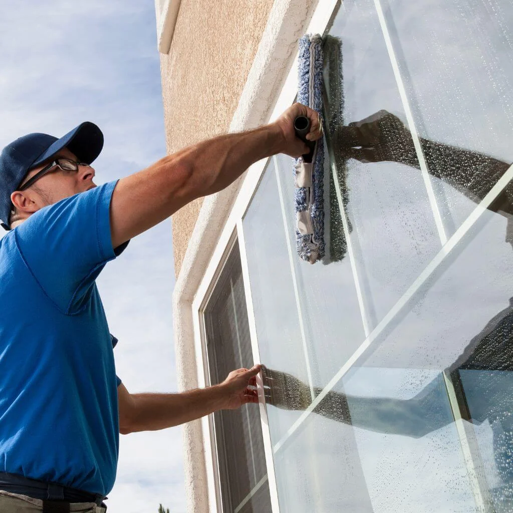A man in blue scrubs a large exterior window.