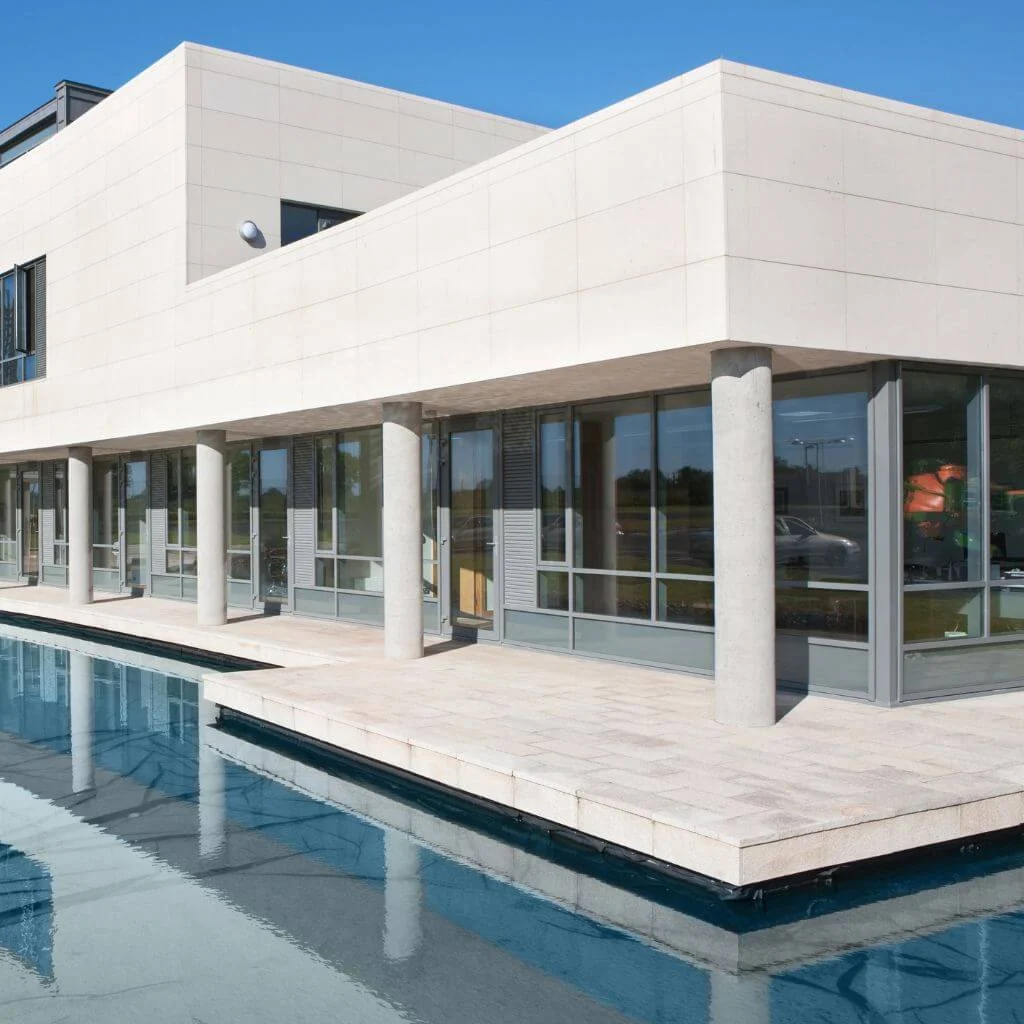 A modern white building stands beside a blue reflecting pool.