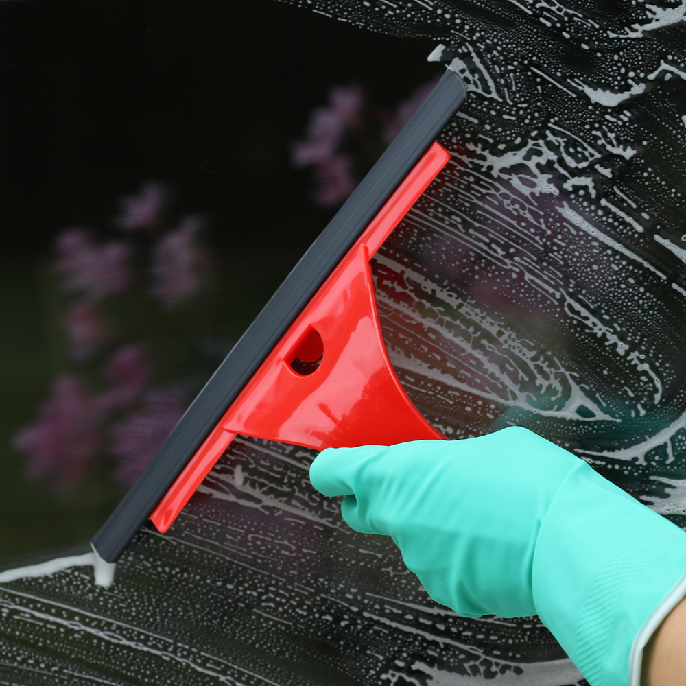 A gloved hand uses a squeegee to clean a soapy window, showcasing window cleaning in Big Spring, Texas. The squeegee has a red handle and gray blade.