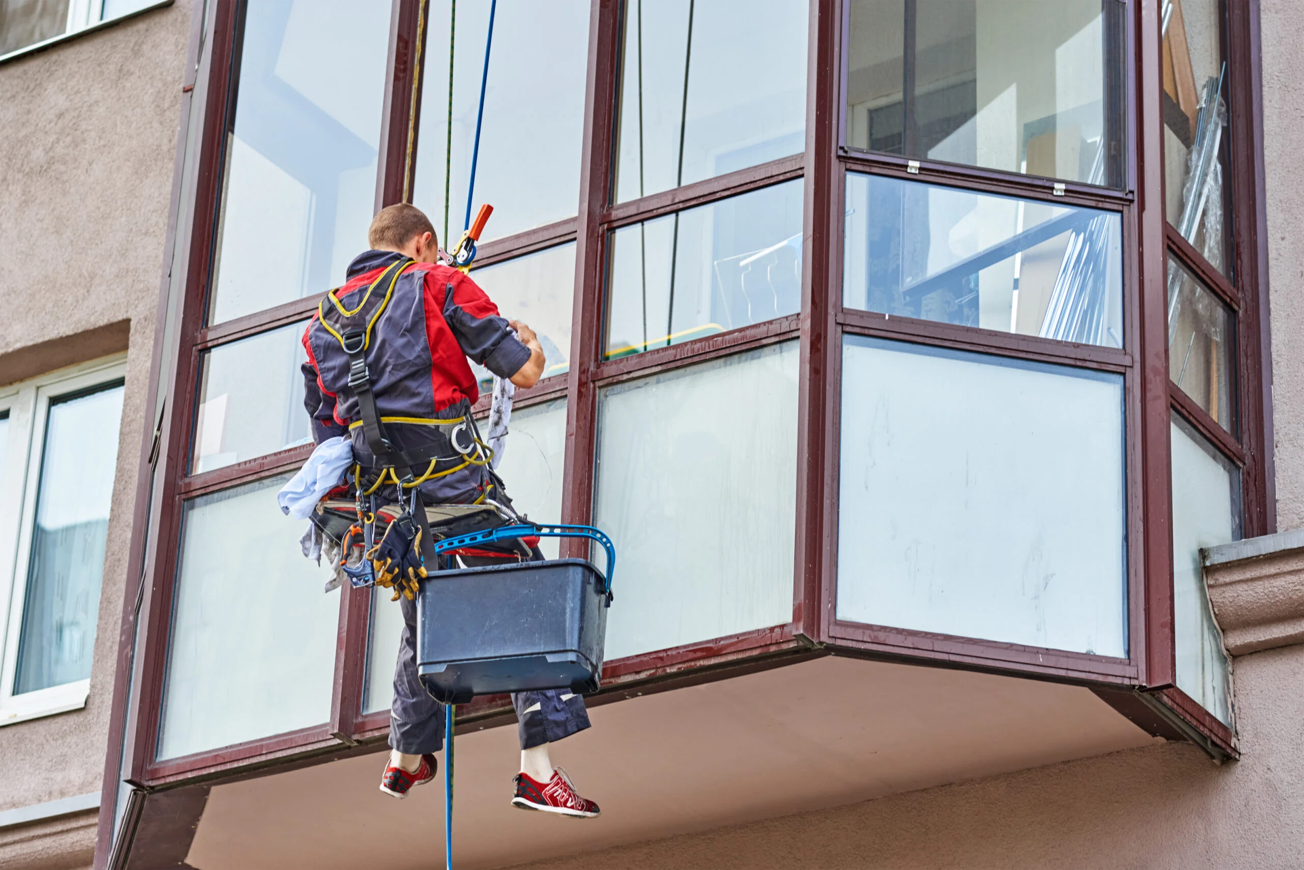 A suspended worker cleans windows on a projecting building bay.